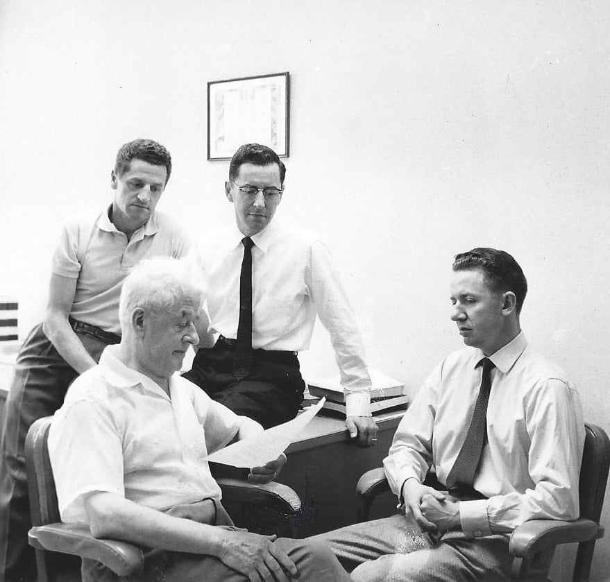 Black and white photo of four men in an office setting